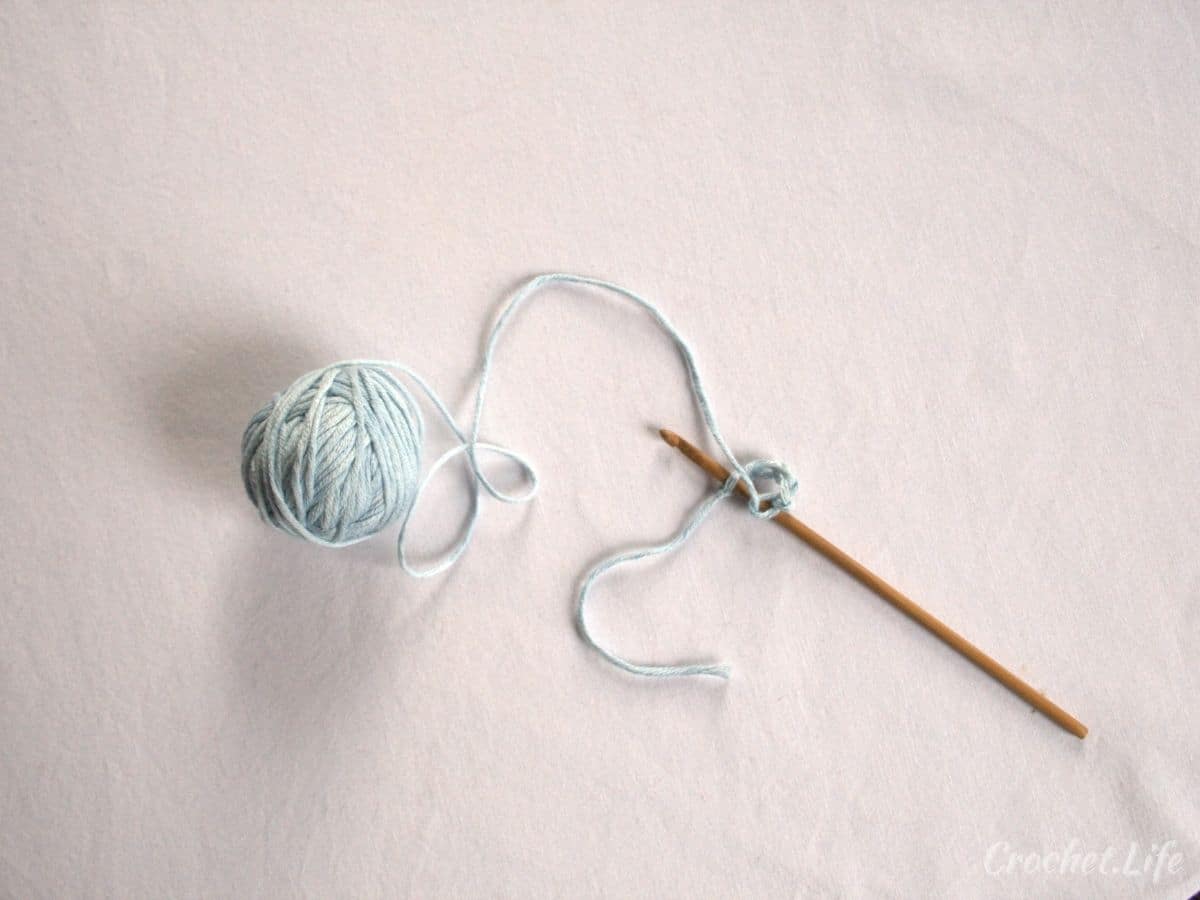 Wooden crochet hook holding blue ball of yarn