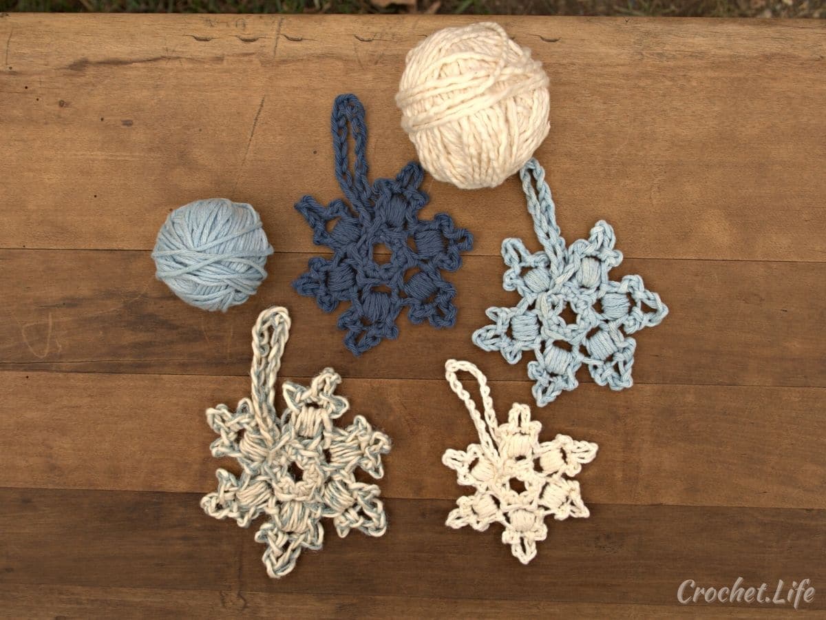 Different shades of blue crochet snowflakes next to balls of yarn