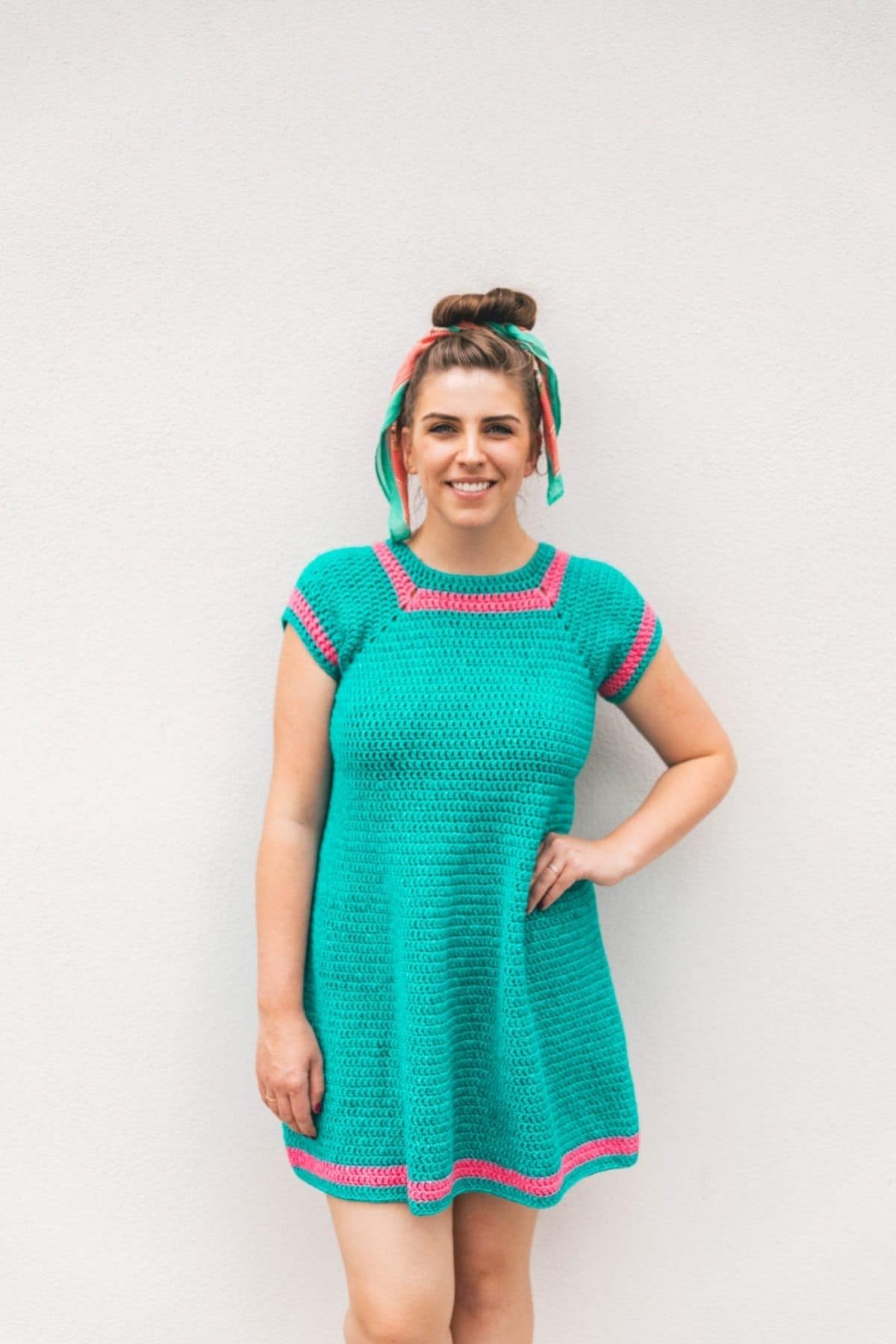 Woman in teal crochet dress against white wall