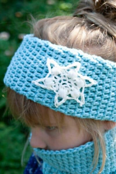 Blonde girl in blue shirt wearing light blue cowl and matching headband with white snowflakes