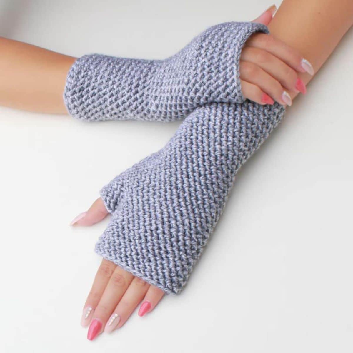 Manicured hands wearing gray fingerless gloves that cover the entire wrist on a white background.