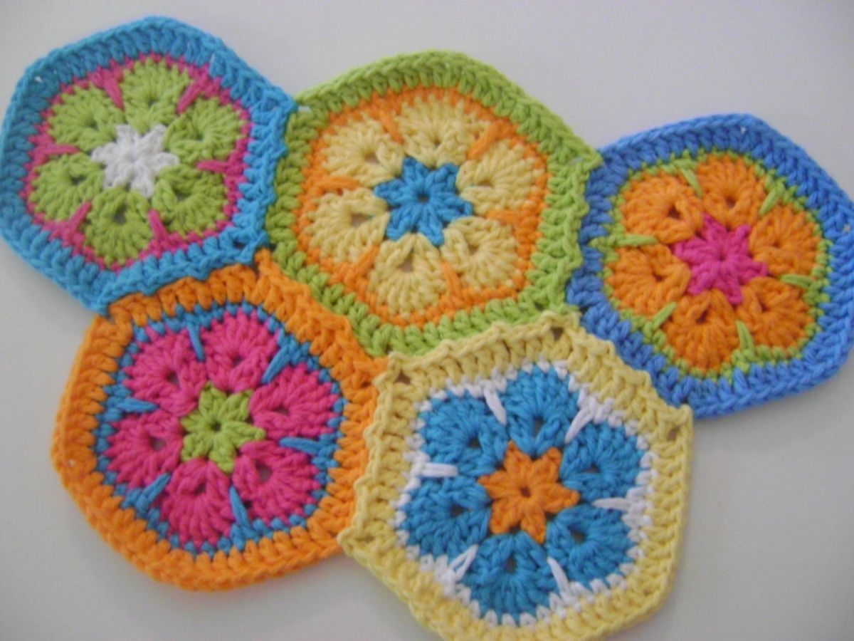 Five crochet hexagon African flowers in pink, blue, orange, and green stitched together with a border around each flower.