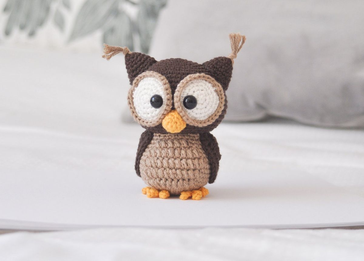 Small brown crochet owl with large white eyes and a small yellow beak standing on a white background.