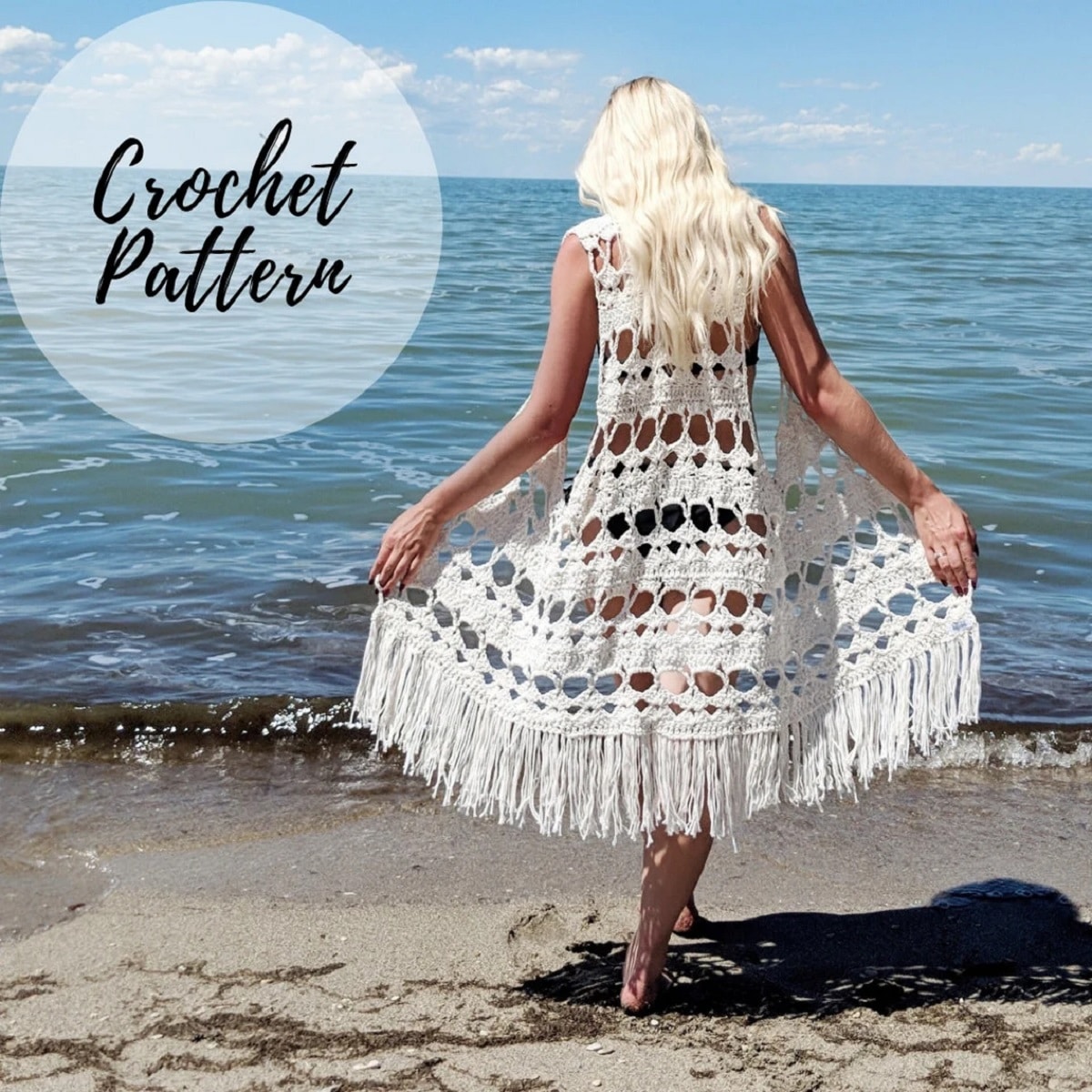 Blond woman staring out to the sea wearing a long white crochet vest with white tassels along the bottom.