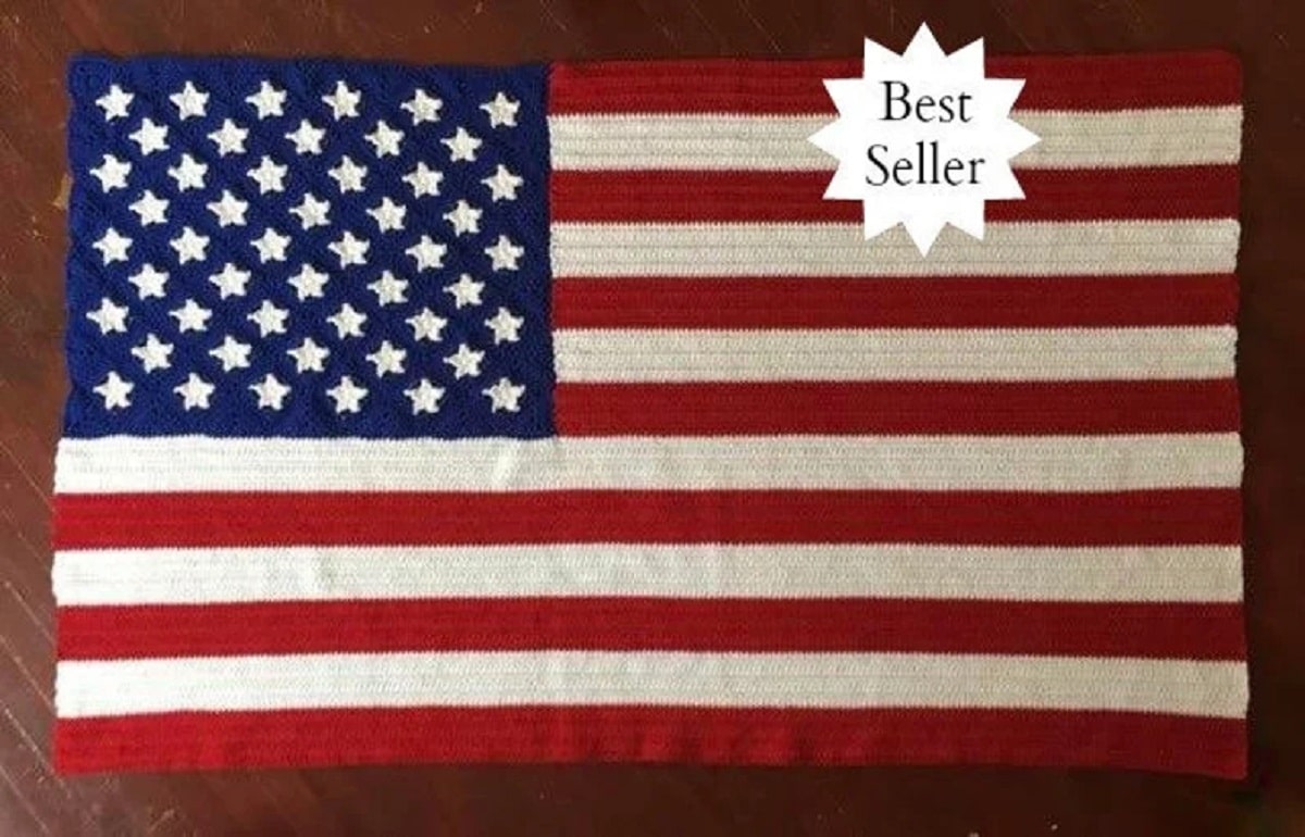 Crochet American flag with intricate stars laid on a dark wooden floor with a best seller sticker in the top corner.