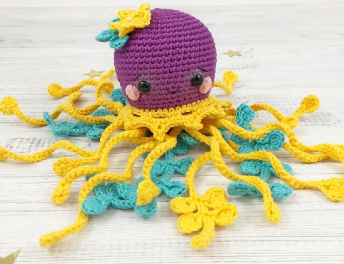 Large purple crochet jellyfish sitting on a light wooden floor with yellow and blue tentacles spilling out around them.