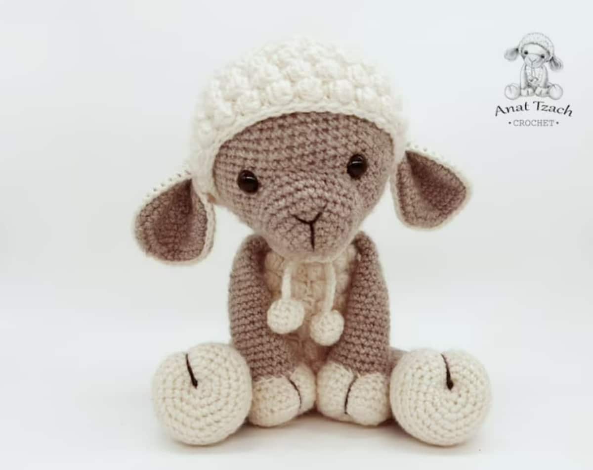 A brown crochet lamb with a white textured cap and body sitting down on a white background.