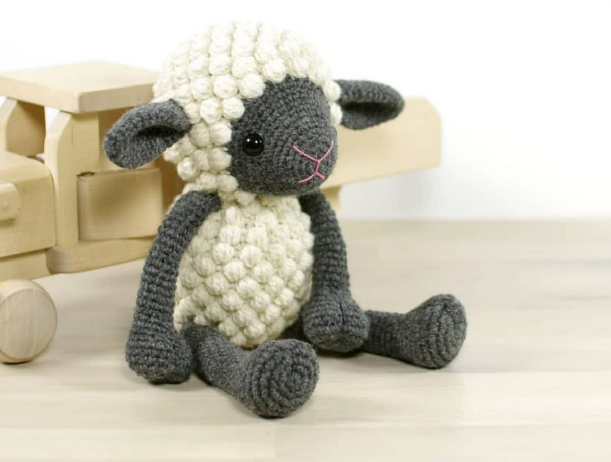 Small crochet lamb with white bobbles over its head and body and gray legs, ears, and face.