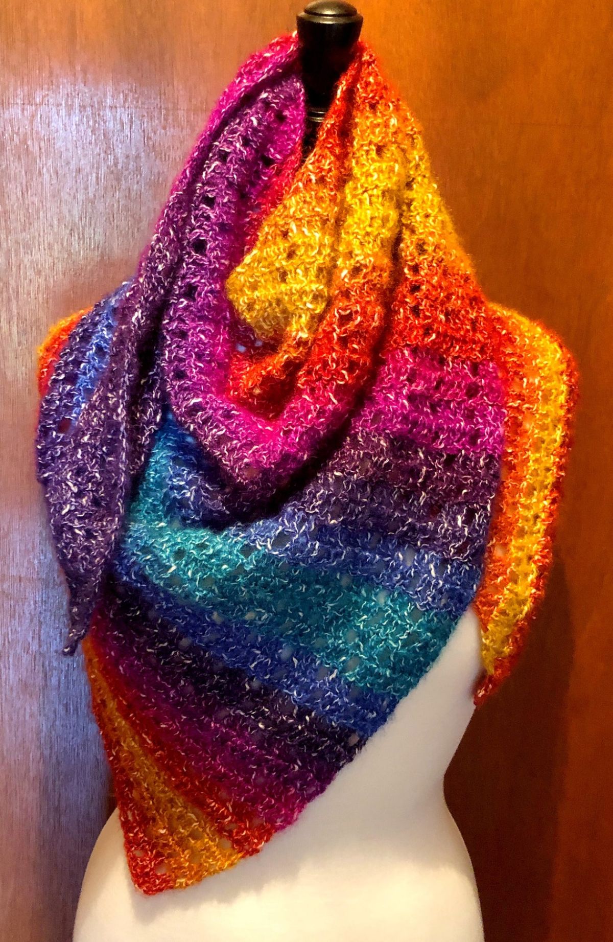 A rainbow colored crochet skein style scarf wrapped around the neck, shoulders, and chest of a white mannequin.