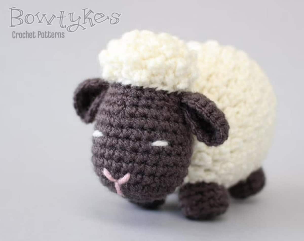 White crochet sheep with a textured body, black ears, legs, and face standing on a white background.