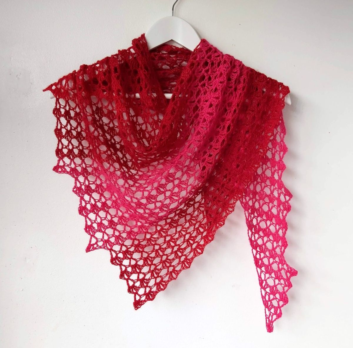Loosely stitched lace style red crochet skein scarf with a slight scalloped edge draped over a white wooden hanger.