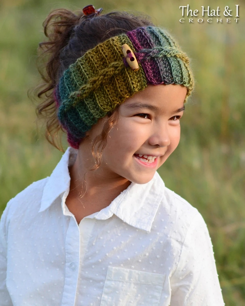 Young girl in a white shirt wearing a blue, green and purple crochet headband with a braid around the center and wooden peg to secure it.