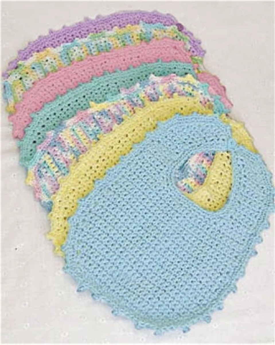 A small pile of crochet baby bibs spread out on a white blanket. The bibs are blue, yellow, pink, green, purple, or a mixture of all colors.