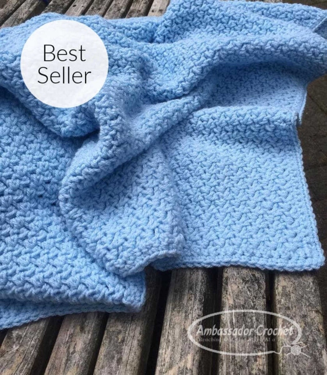 Baby blue crochet blanket scrunched up and folded on a wooden background with best seller written in a bubble in the top corner. 