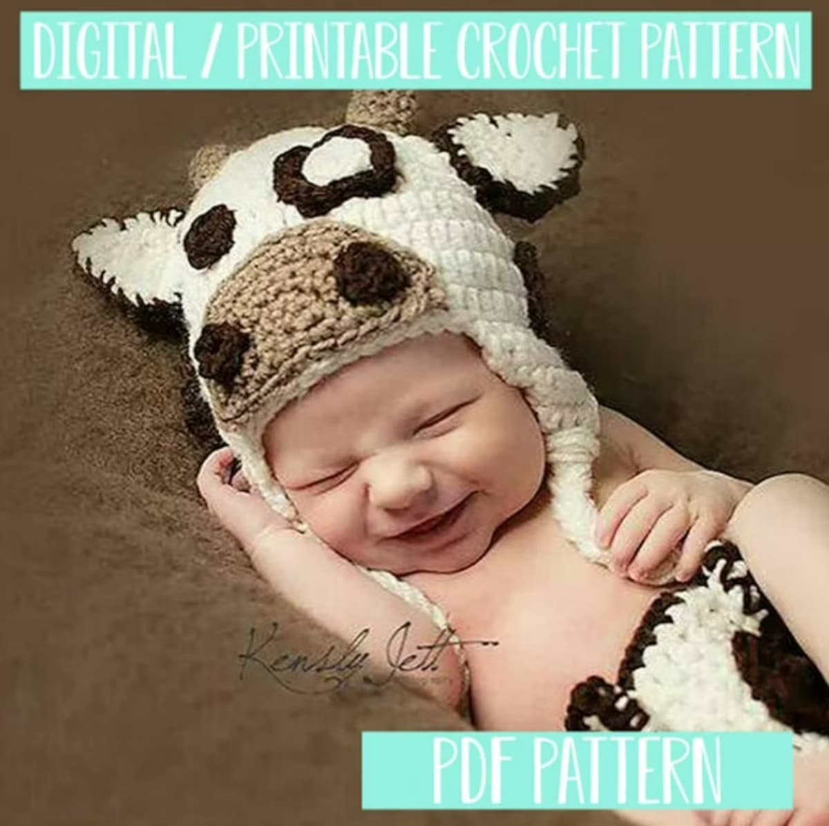Newborn baby on a brown cushion wearing a white and brown crochet cow’s hat with white earflaps and a matching diaper cover.