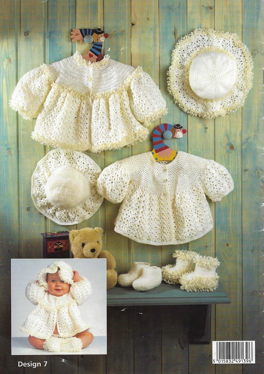A white crochet cardigan with a yellow ruffle on the bottom hanging next to two white bonnets and a white dress with half sleeves.
