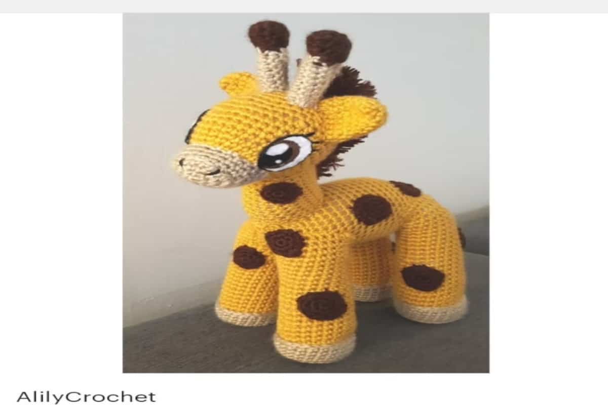 Bright yellow baby style crochet giraffe on four legs with large eyes and brown circles on its body and legs on a white background.
