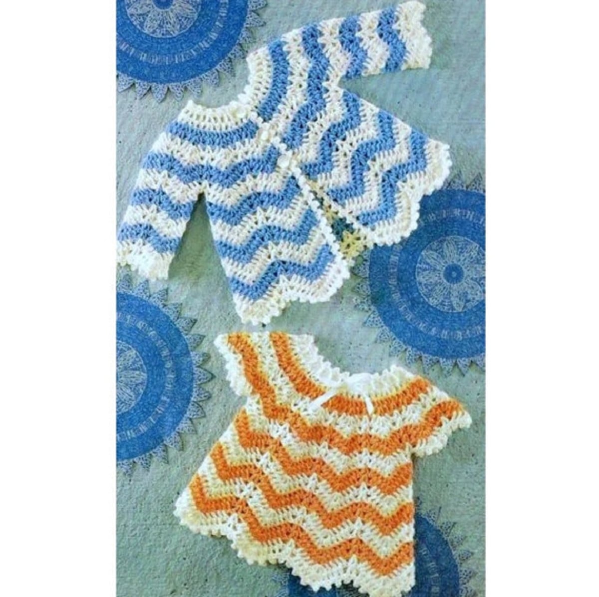A blue and white zig zag crochet baby cardigan next to an orange and white crochet dress with the same pattern.
