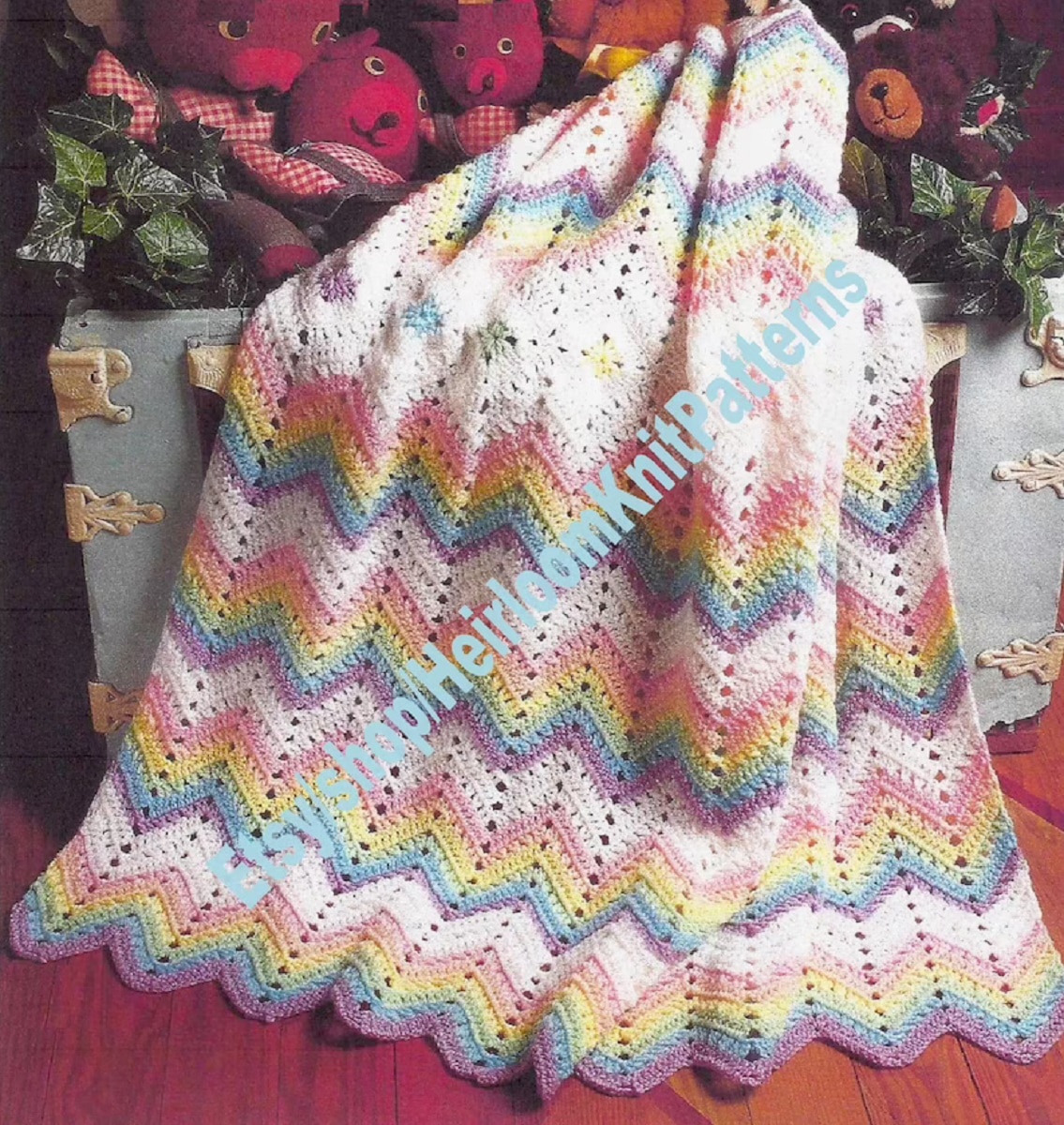 Rainbow colored crochet Afghan with zig-zag horizontal stripes of color and a zig-zag trim on the bottom on a red background.