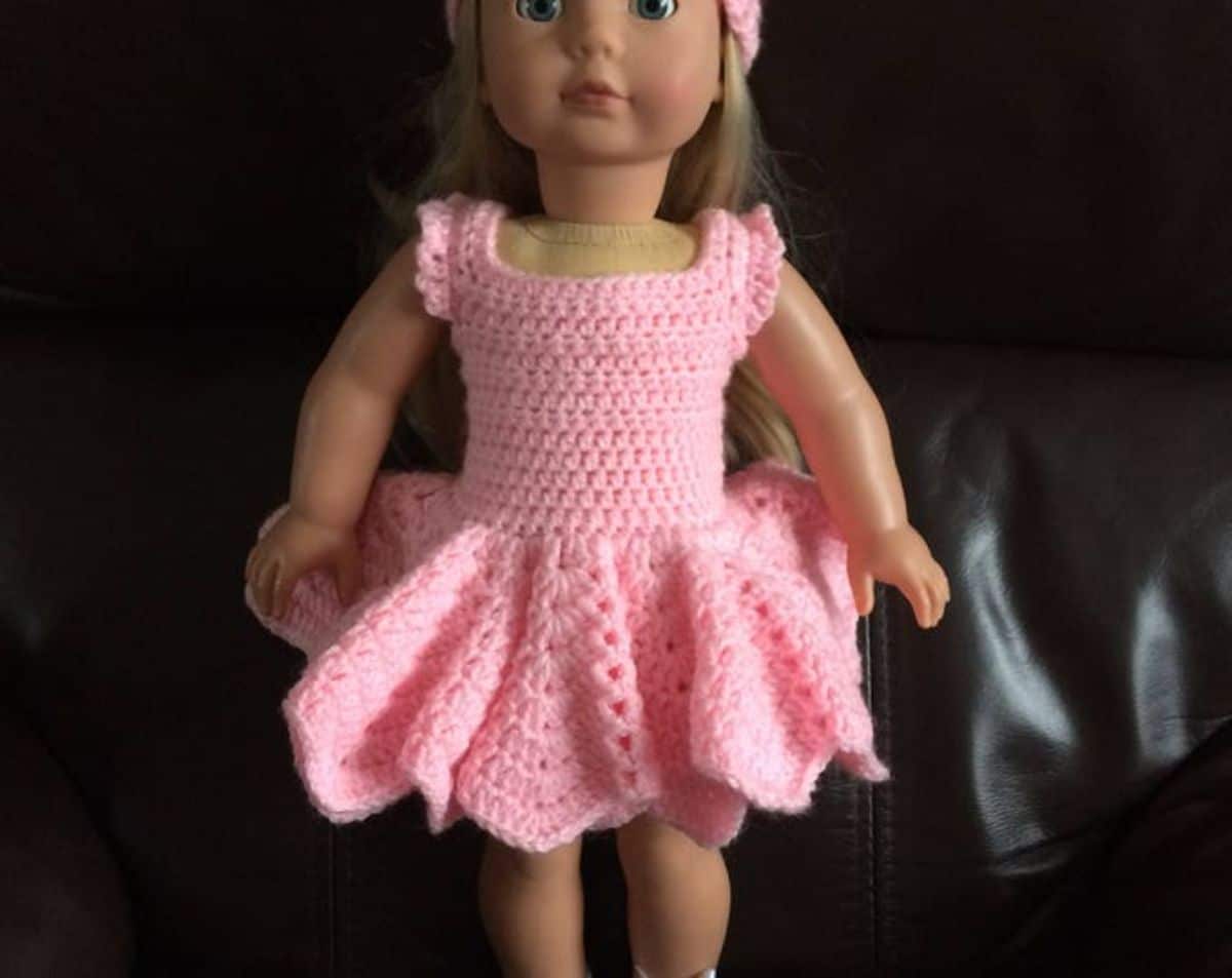 Blonde doll wearing a pink crochet ballerina dress with a puffy tutu standing against a black background.