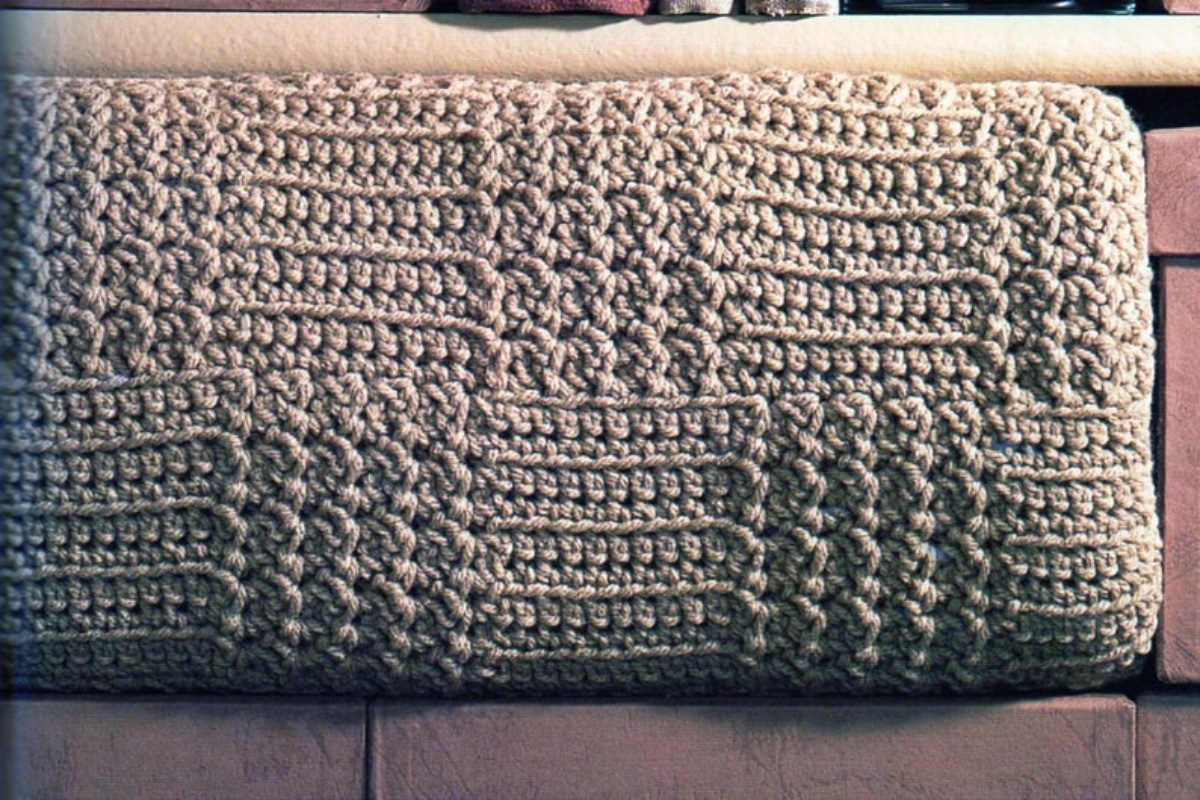 Gray basketweave crochet blanket folded into a rectangle and placed on a couch.
