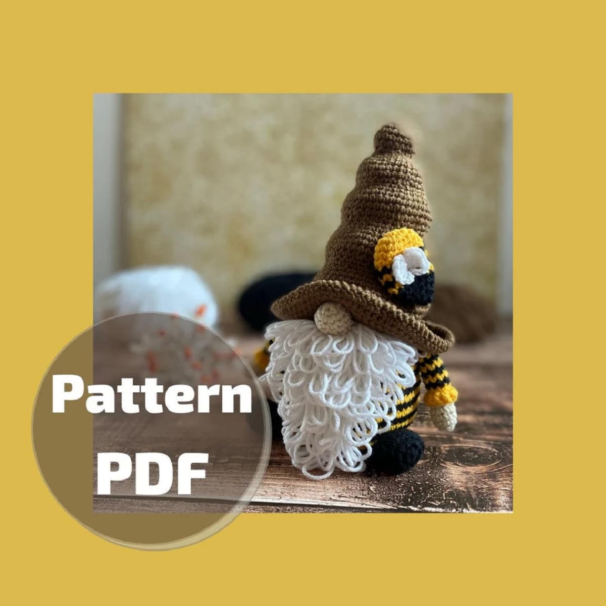 Crochet gnome with a large brown pointed hat with a bumble bee on and long white loosely weaved beard poking out.