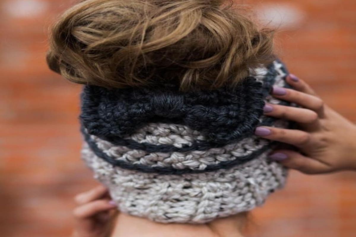 The back of a brunette woman wearing a cream crochet hat with a bun pulled through and a large navy blue bow underneath the bun.