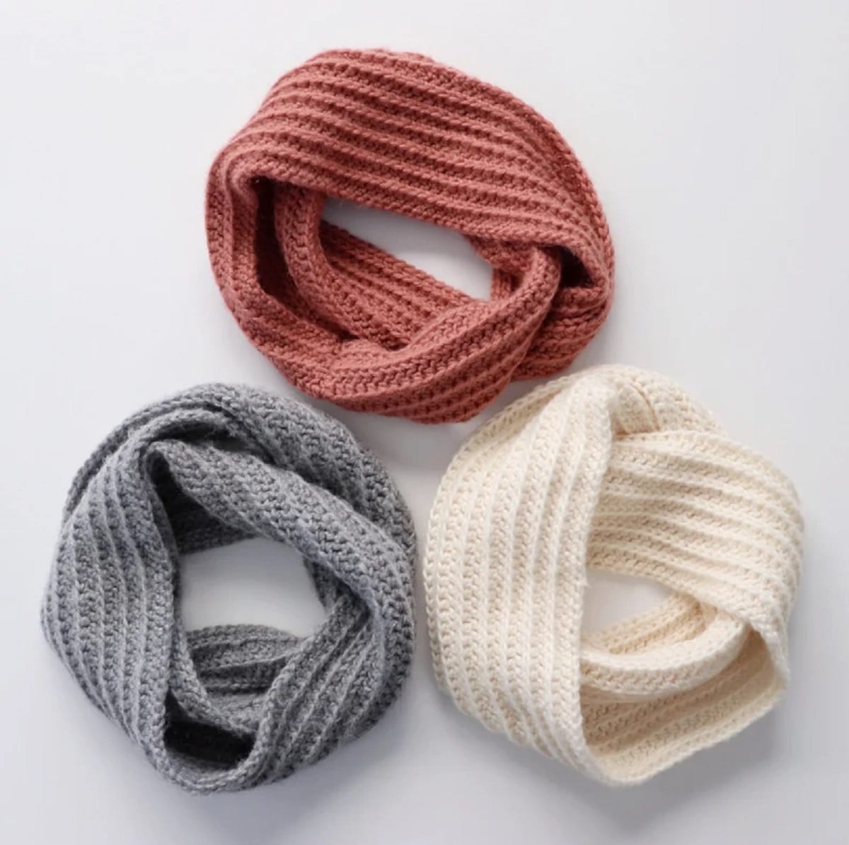 A cream, orange, and gray crochet infinity scarf placed in three circles on a white background. 