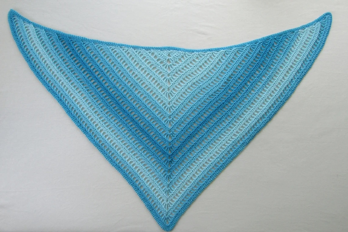 A light blue and dark blue diagonal striped crochet triangle shawl on a white background.