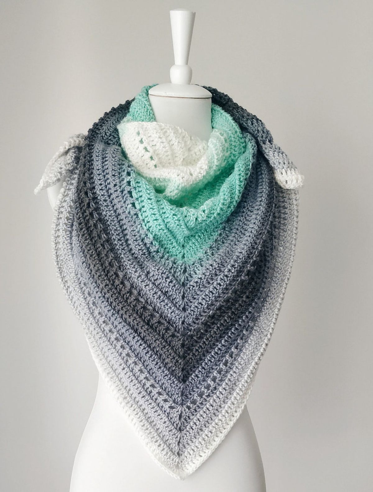  White, grey, and green crochet skein shawl with diagonal lines for each color wrapped around the mannequin's neck on a white background.