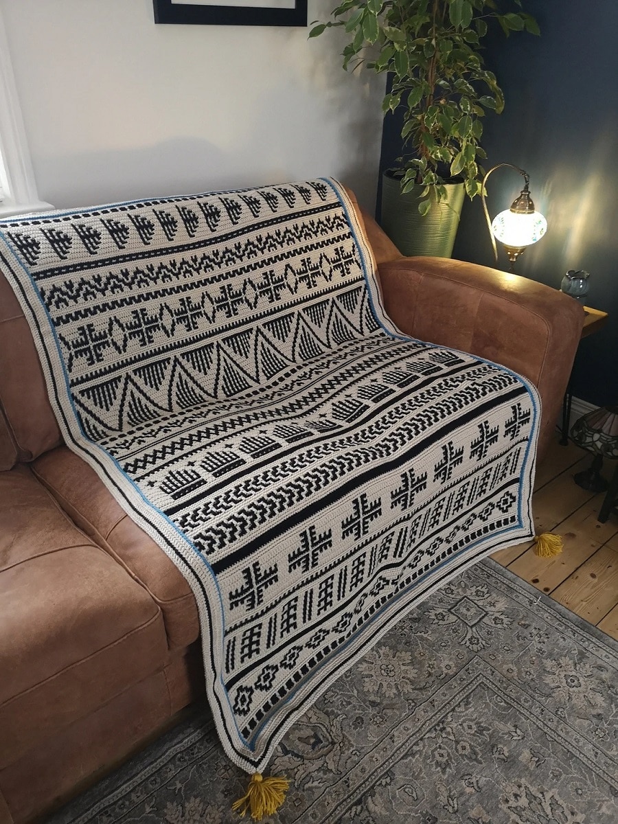 Black and white striped crochet Afghan with diamond, cross, and striped patterns draped over a brown couch.