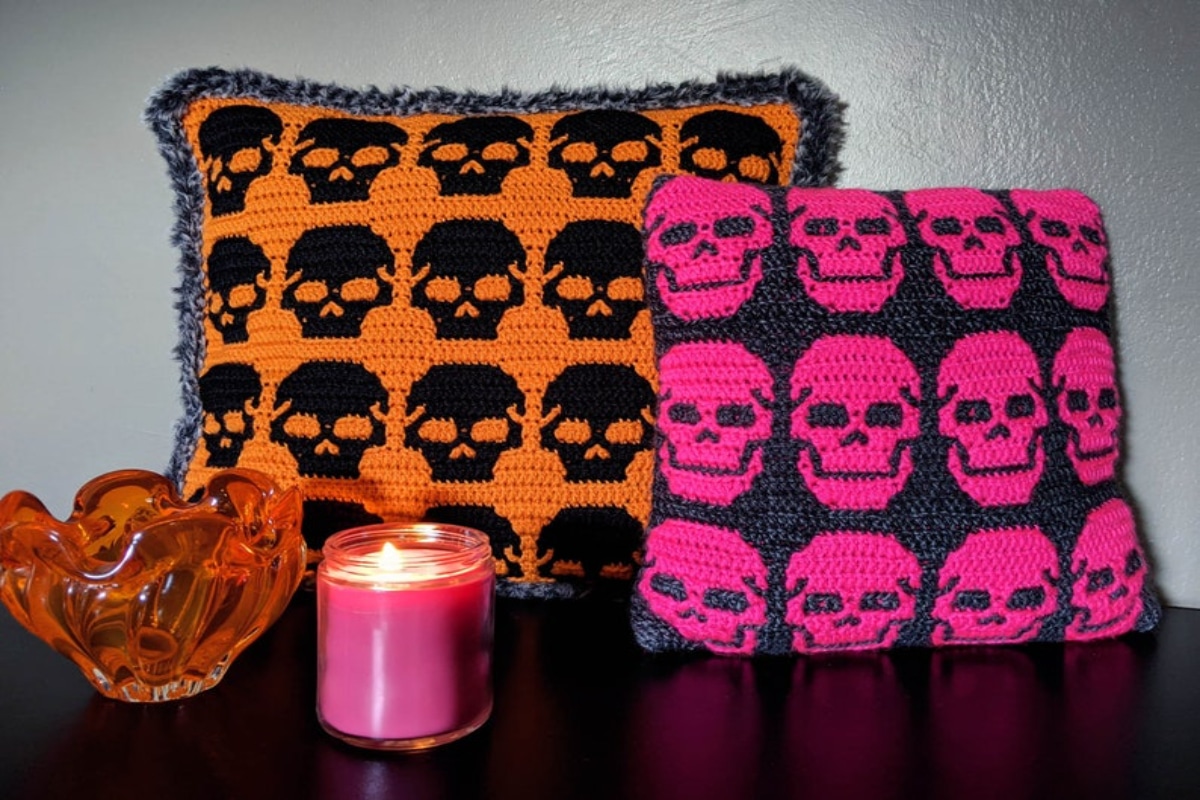 An orange crochet cushion with a black skull pattern all over and a black cushion with a pink skull pattern across it.