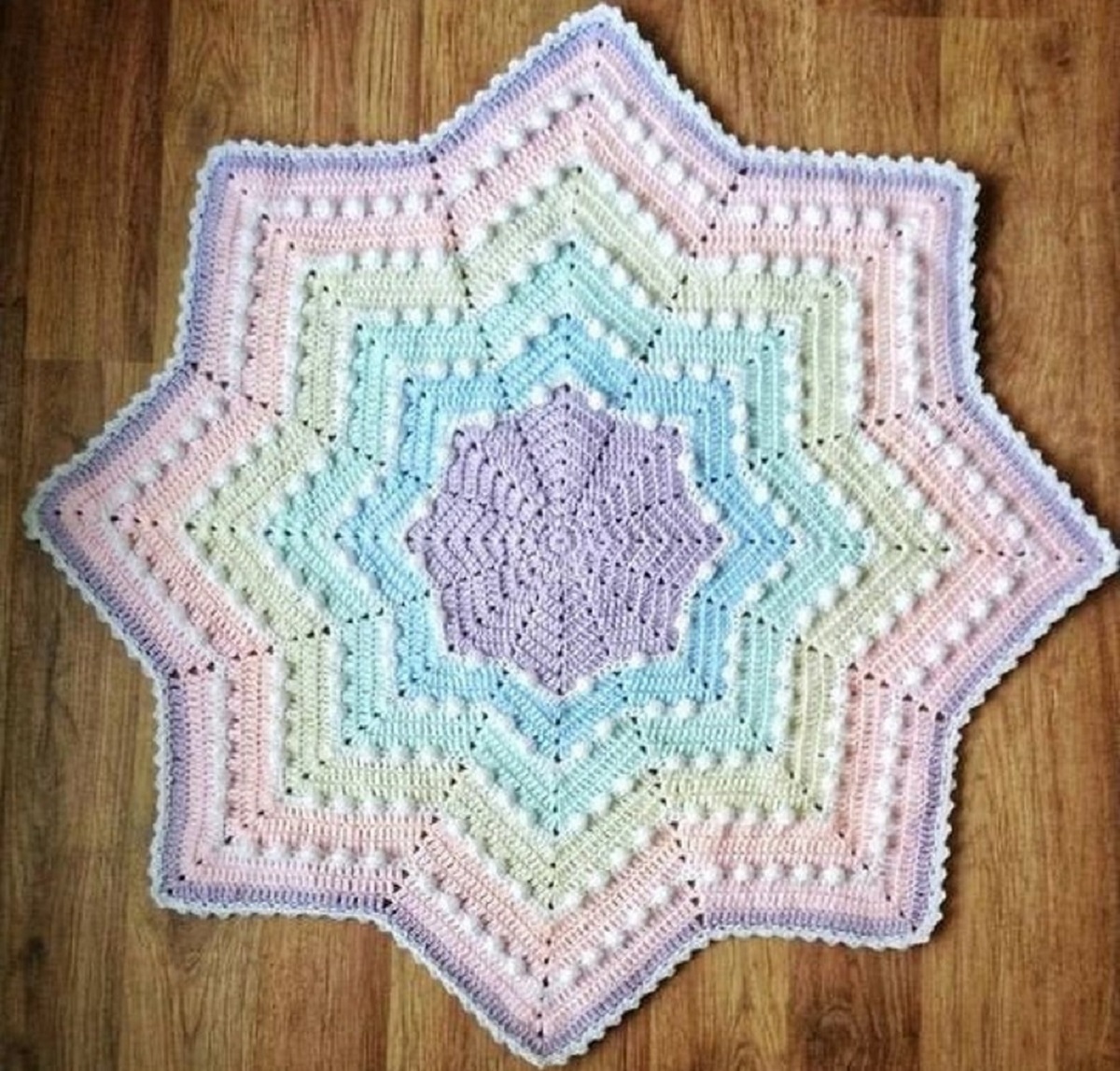Pastel pink, purple, yellow, and blue star shaped crochet blanket with small white bobbles around each row of color.