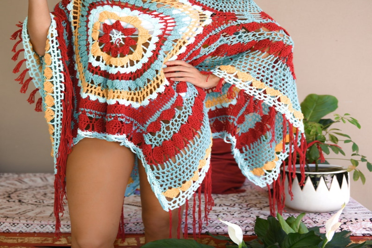 Woman wearing a blue, orange, and yellow oversized poncho with tassels along the bottom and a large mandala in the center.