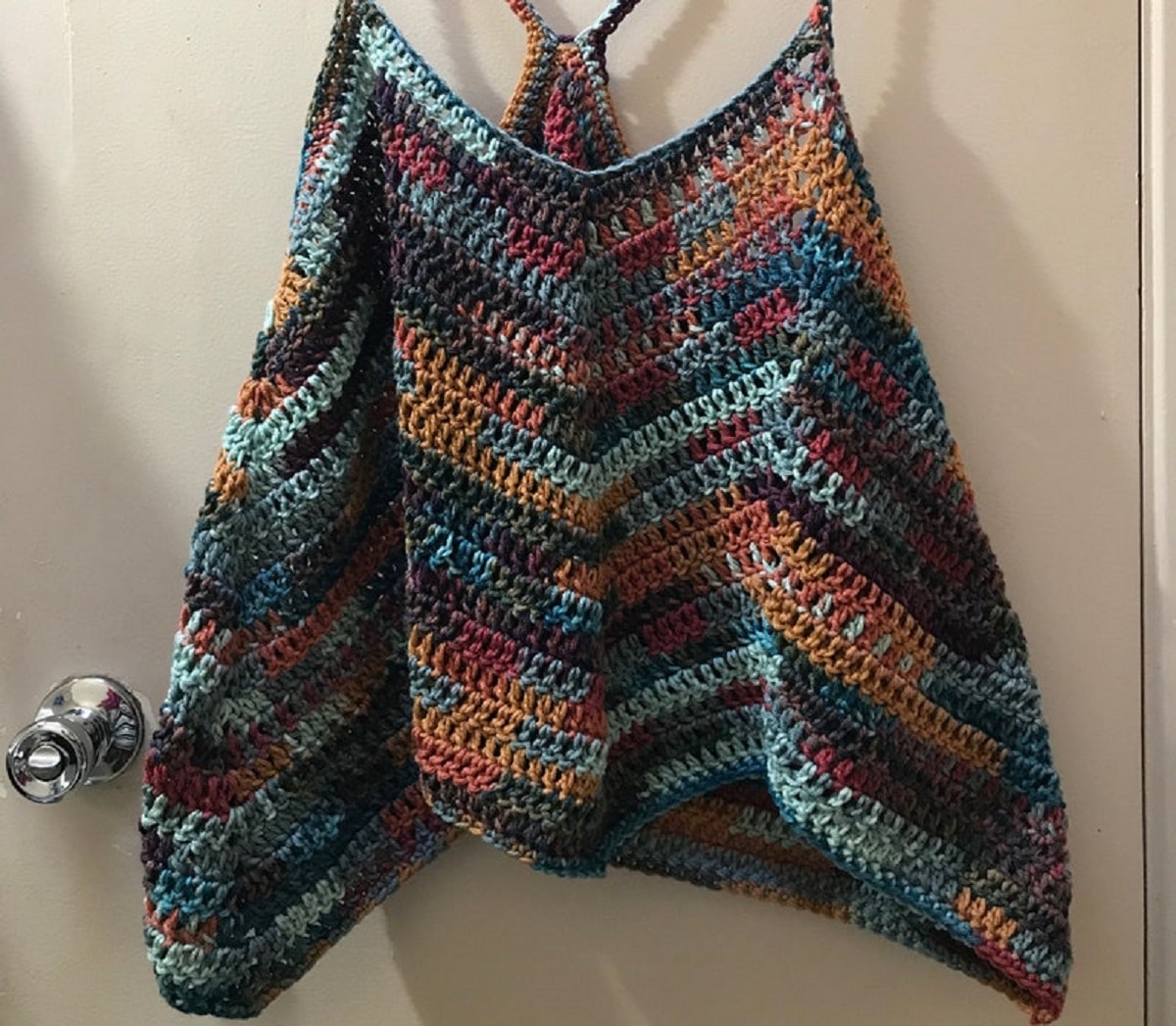Blue, green, orange, and purple striped crochet tank top with thin straps hanging on the back of a door.