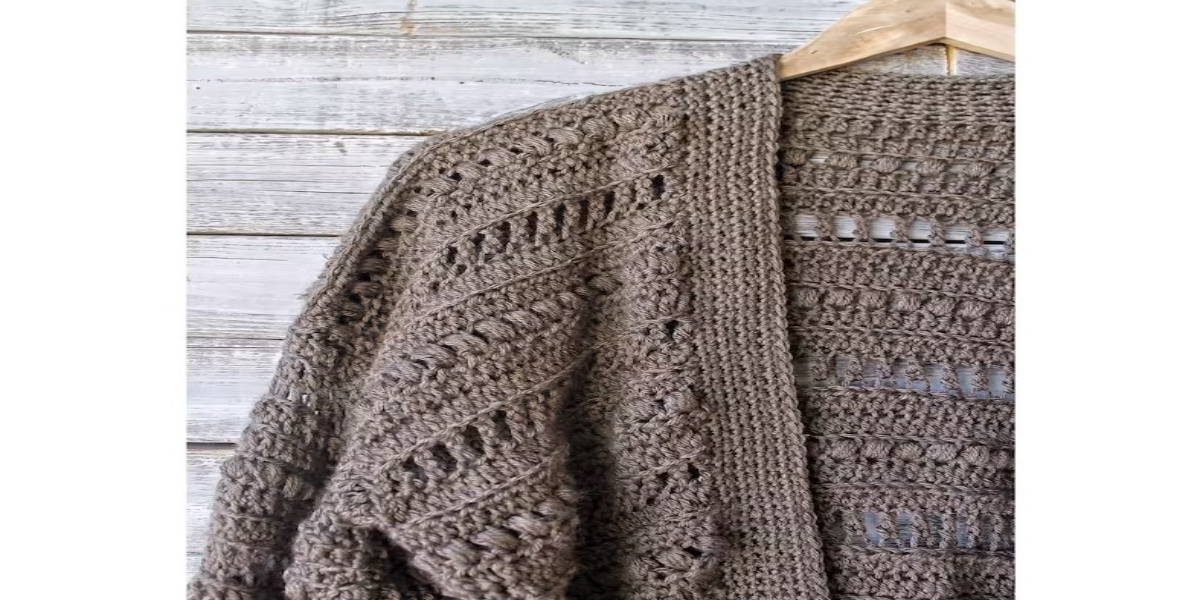 A light brown crochet lacy cardigan on a pale wooden hanger lying on pale wooden floorboards.