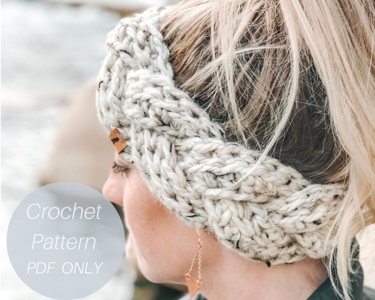 Blond woman side profile wearing a cream crochet ear warmer with braided design against a white snowy background.