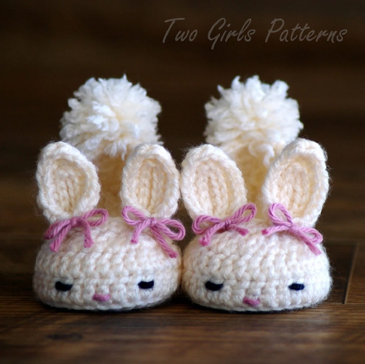 White crochet baby boots with a bunny face, ears with pink bows attached, and a fluffy tail on the back of the boots.