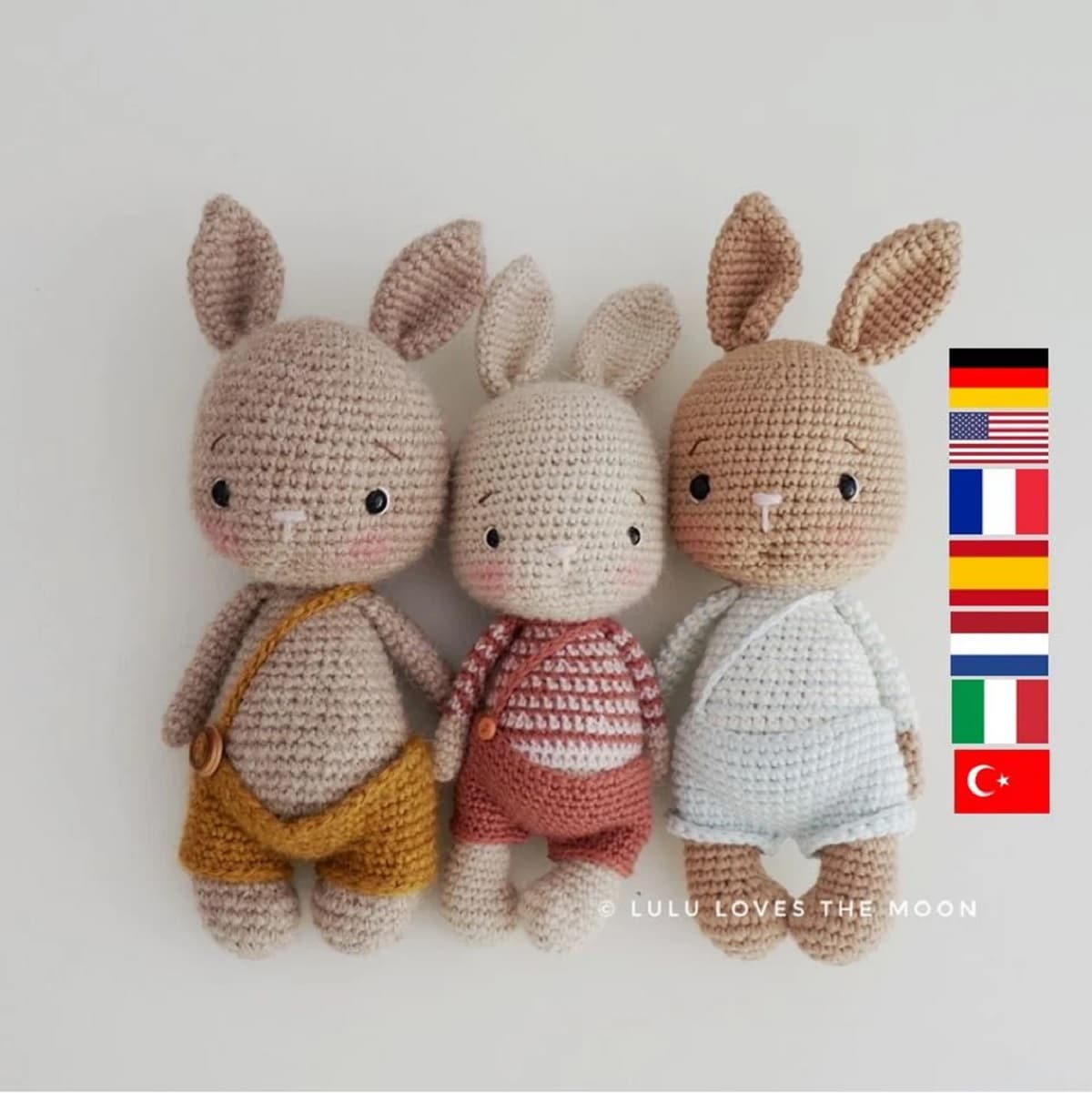 Three brown crochet bunnies standing in a line wearing small shorts with braces and buttons to hold them in place.