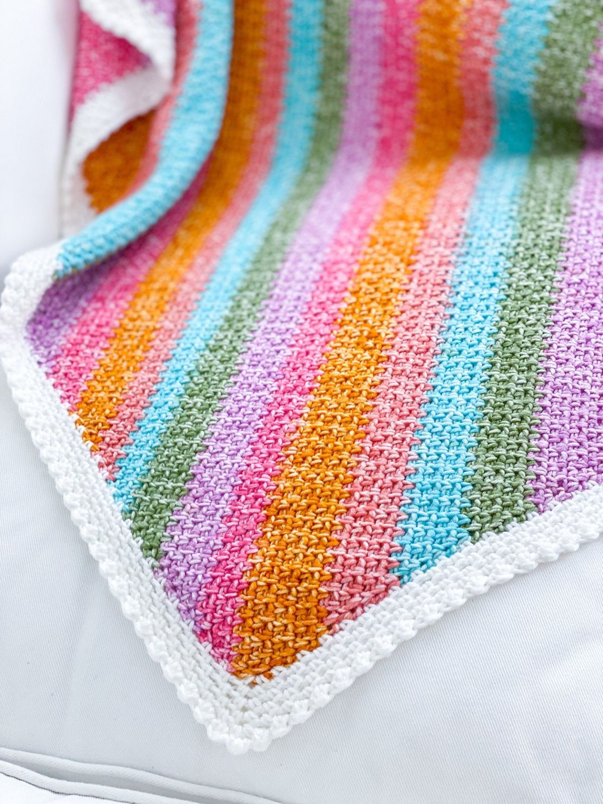 A pink, blue, orange, purple, and green vertical striped crochet blanket with a white bobble border on all sides.