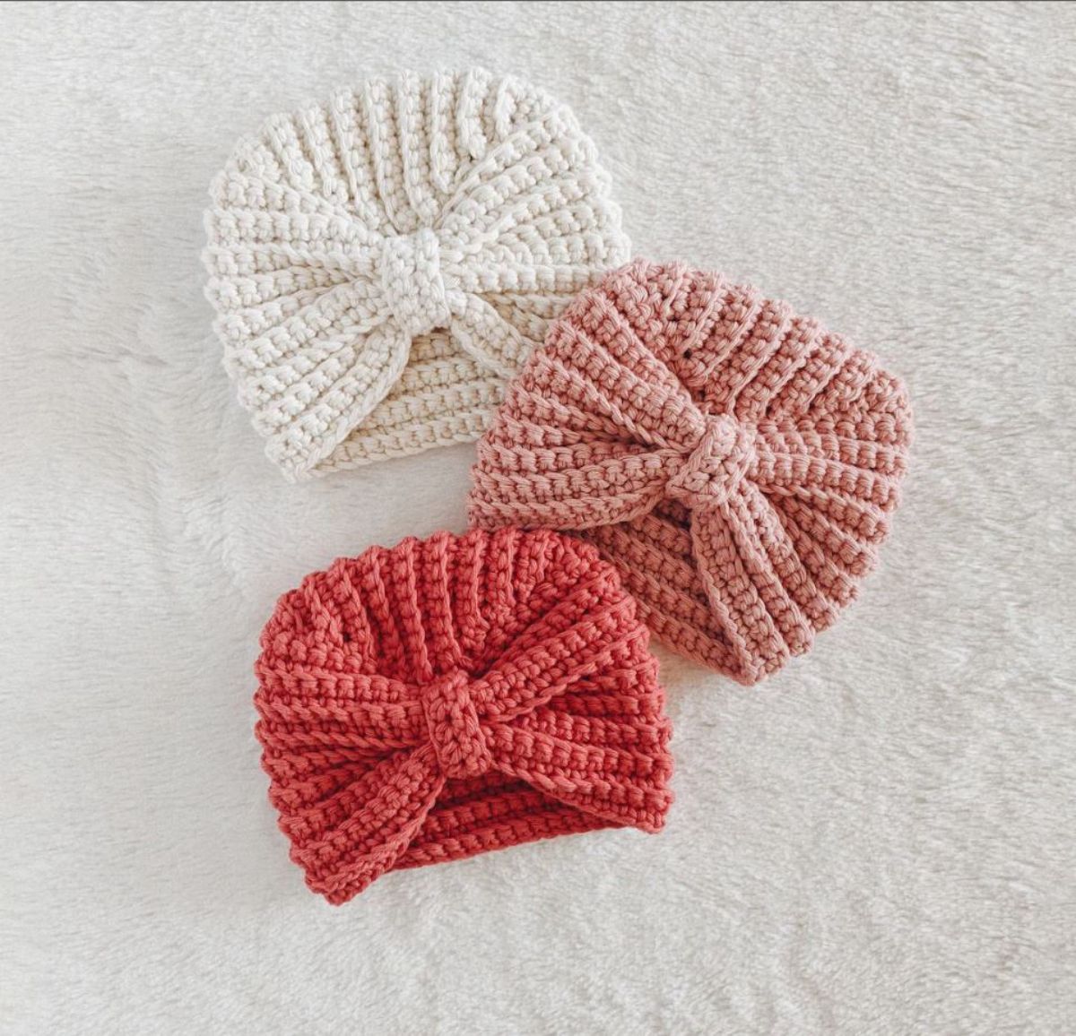 Pink, pale pink and cream beanies with a turban style bow in the center on a white background.