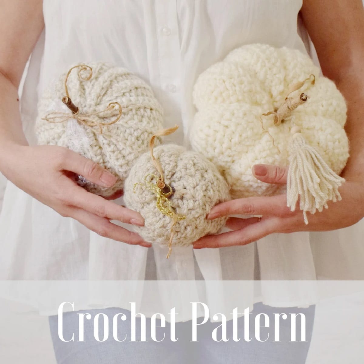 A woman in white holding three white crochet pumpkins in her arms.