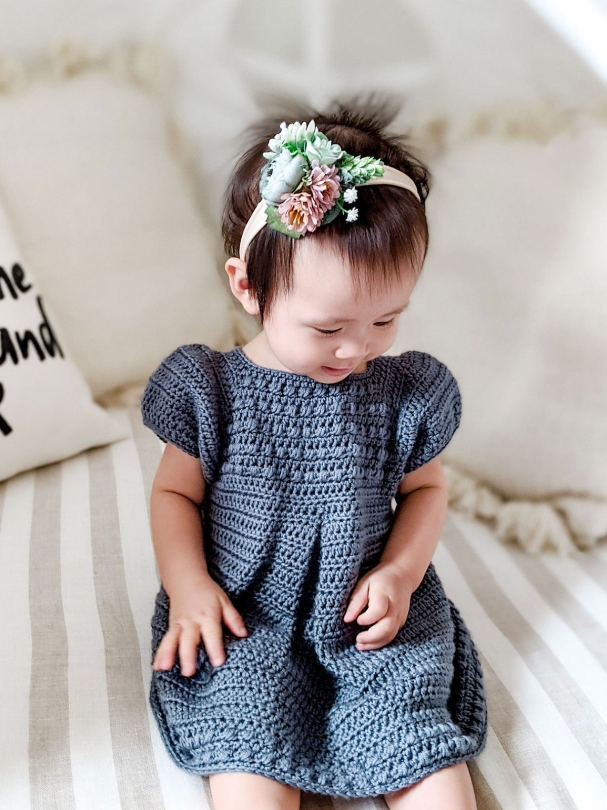 Dark haired toddler wearing a navy capped sleeve crochet dress with a high neck and a floral headband.