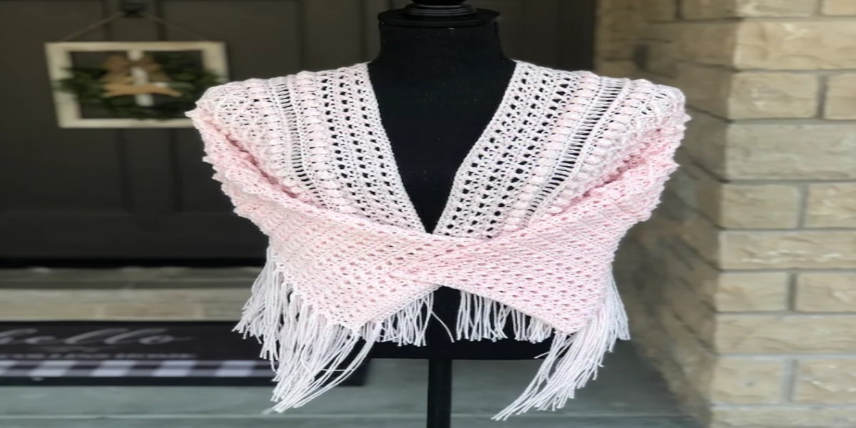 A white and pink crochet cardigan with tassels along the bottom on a black mannequin.