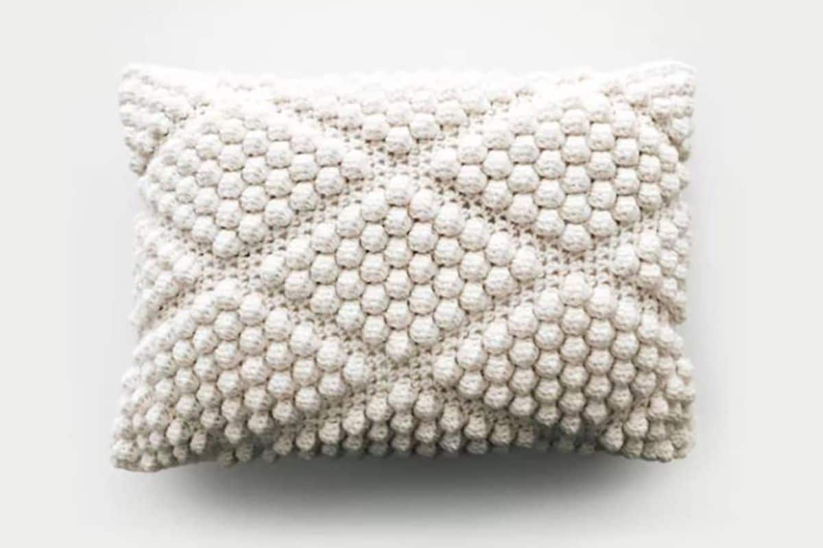 Rectangle shaped cream cushion with diamond bobble style crochet pattern on a white background. 