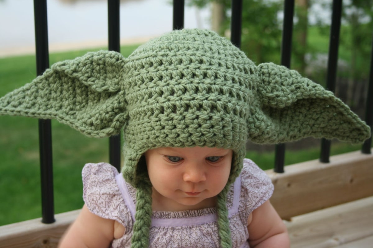  Young girl wearing a green crochet baby Yoda hat with large ears either side and green braided earflaps.