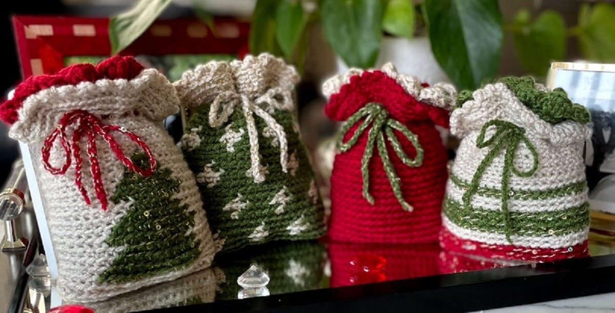 Four crochet Chrisrmas gift sacks in red, green, and cream with Christmas trees or stripes attached to the front.