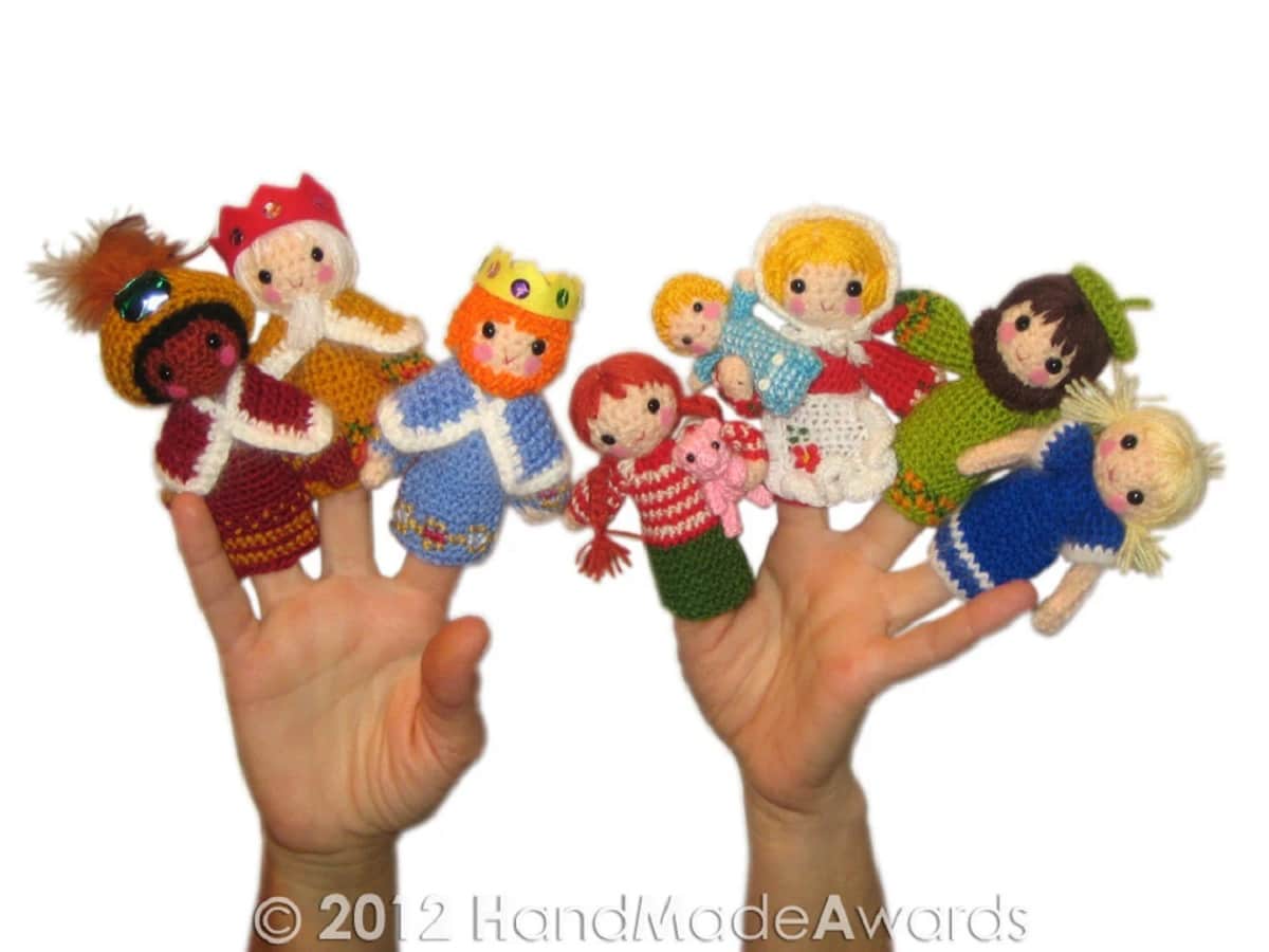  Two hands wearing crochet finger puppets of all the members of the nativity on a white background.