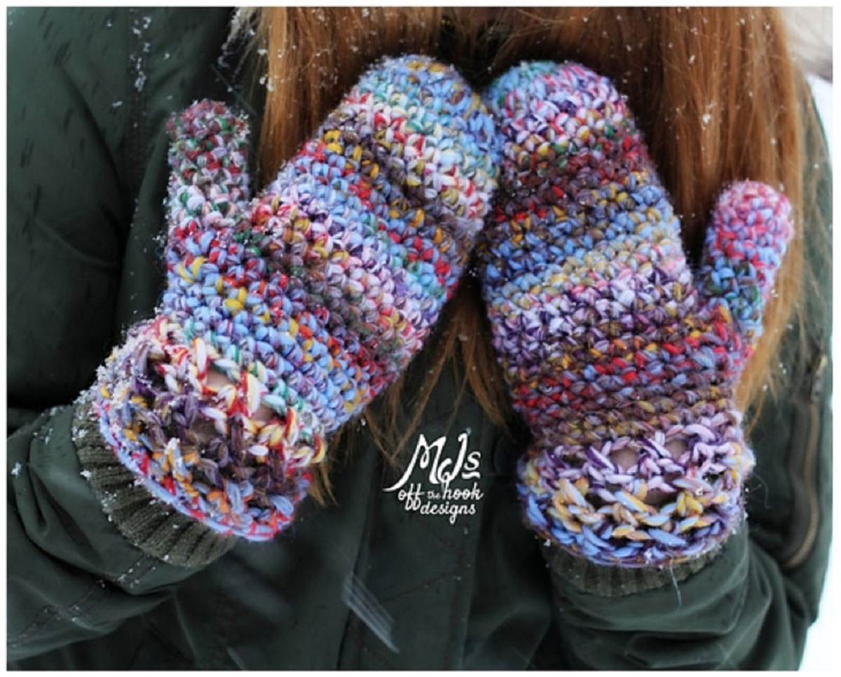  Chunky crochet multi-colored mittens with a loose weave worn by a brunette woman placing her hands on her black coat.