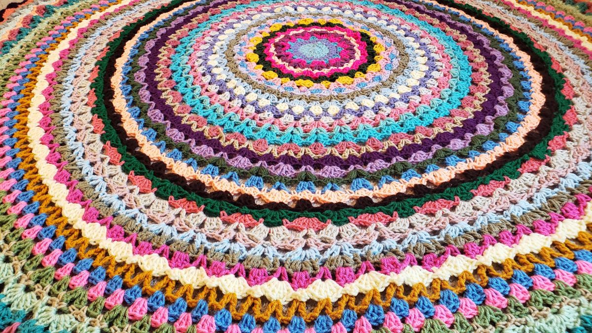  Multi-colored round crochet blanket with round rows increasing in size containing small stitches of each different color.
